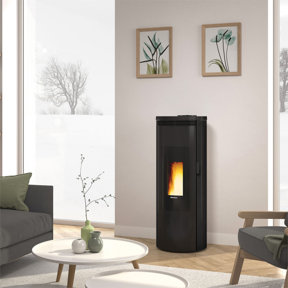 Ambientebild: Extraflame Pelletofen AMIKA EVO in Schwarz mit abgerundeten Seiten, Sichtfenster und Flamme, im hellen Wohnzimmer mit Sofa und Tisch | Klimaworld.com