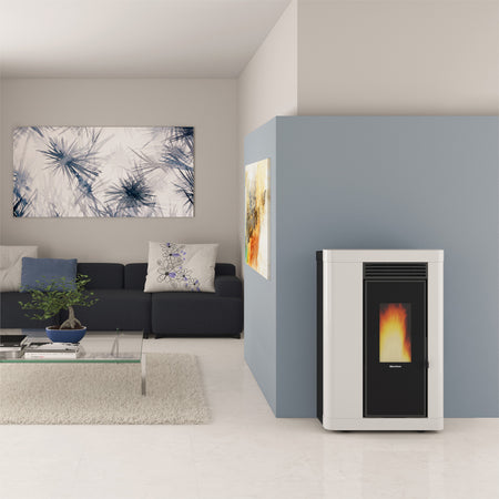 Ambientebild: schmaler Extraflame Pelletofen ANNABELLA AD EVO in Weiss; im Wohnzimmer vor blauer Wand, Sofa, Bild und Glastisch | Klimaworld.com
