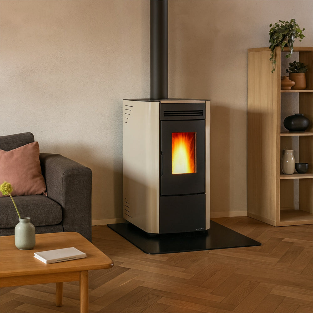 Ambientebild: Extraflame beluefteter Pelletofen KETTY 5.0 in Creme mit schwarzer Front und Sichtfenster, auf Glasplatte im Wohnraum neben Sofa und Holzregal | Klimaworld.com