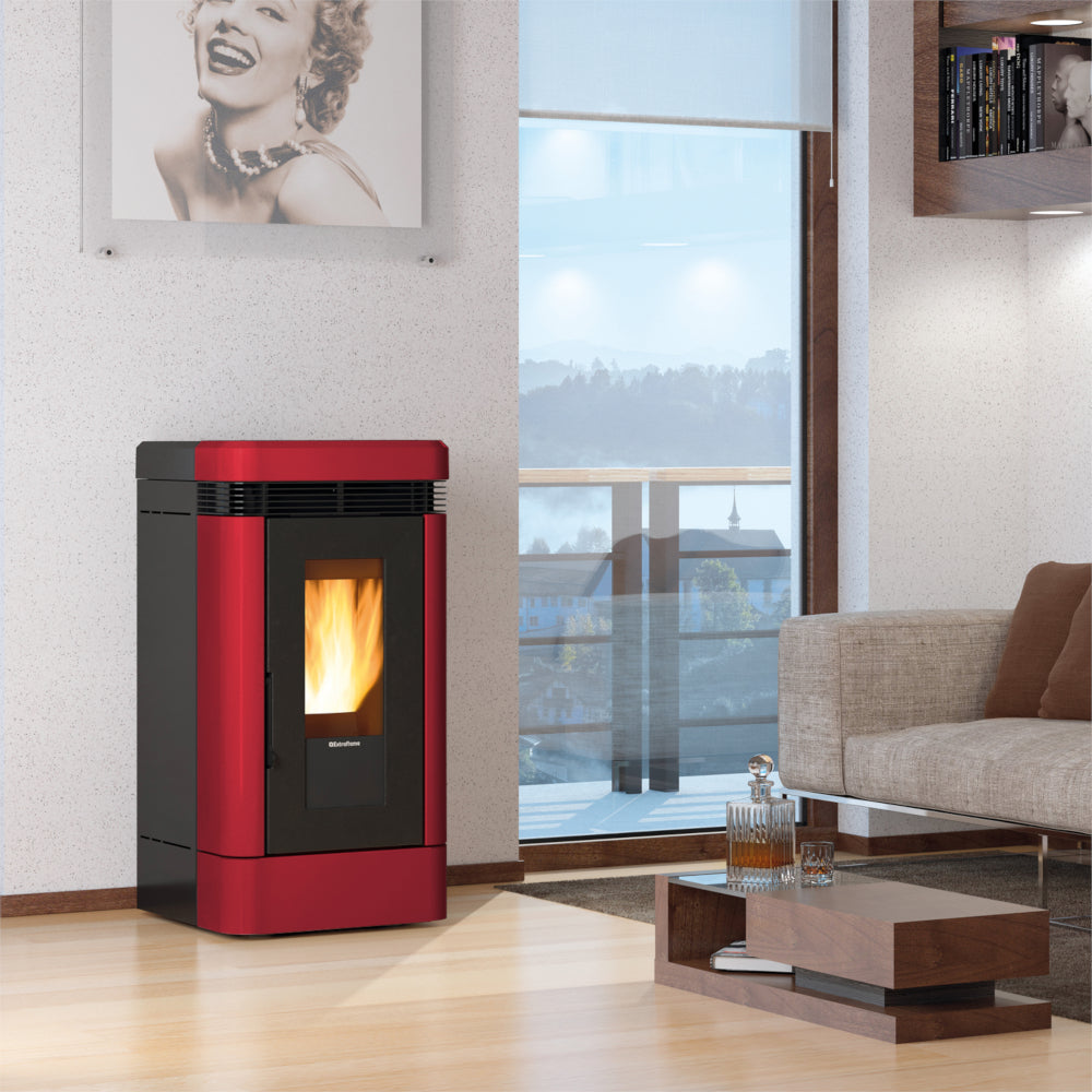 Ambientebild: Extraflame Pelletofen LUCIA.16 in Bordeaux im Wohnzimmer neben Fenster, Flamme sichtbar, Sofa und Couchtisch im Raum | Klimaworld.com
