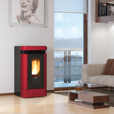 Ambientebild: Extraflame Pelletofen LUCIA.16 in Bordeaux im Wohnzimmer neben Fenster, Flamme sichtbar, Sofa und Couchtisch im Raum | Klimaworld.com

