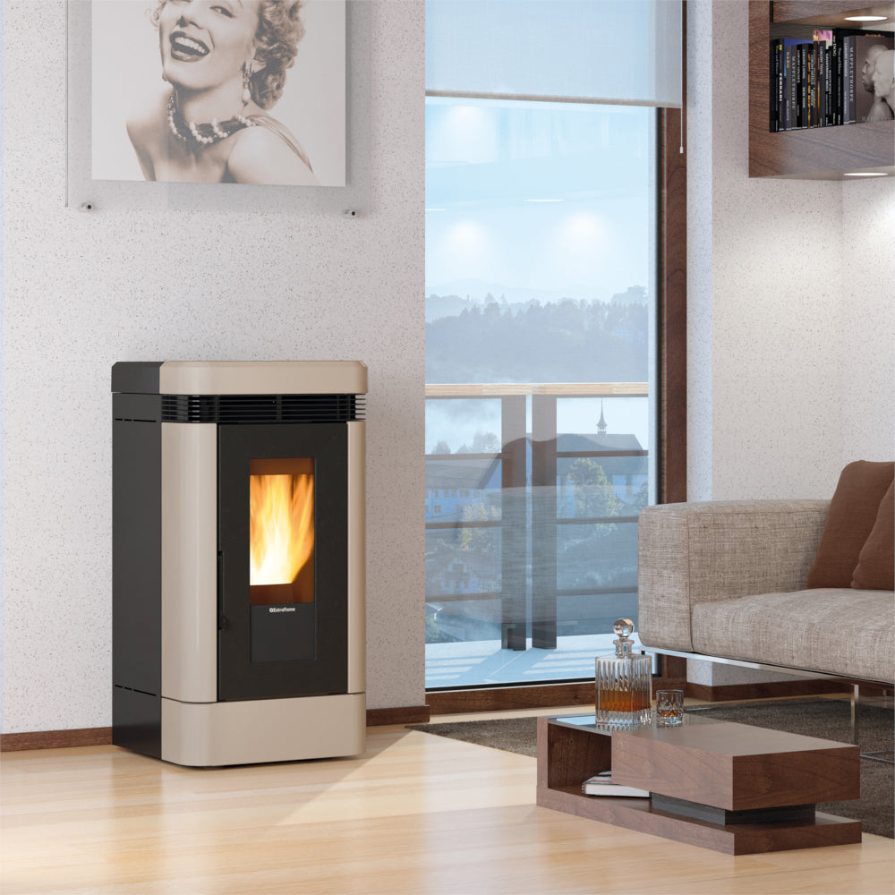 Ambientebild: Extraflame Pelletofen LUCIA.16 in Taupe im Wohnzimmer neben Fenster, Flamme sichtbar, Sofa und Couchtisch im Raum | Klimaworld.com
