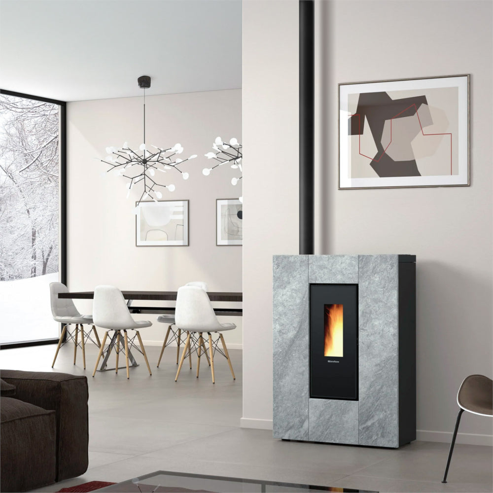 Ambientebild: schlanker Extraflame kanalisierter Pelletofen MARILENA PLUS Petra 5.0.16 mit Natursteinverkleidung vor heller Wand im Wohnraum mit Flamme | Klimaworld.com