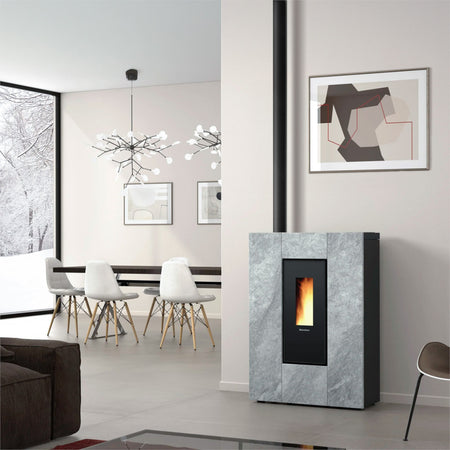 Ambientebild: schlanker Extraflame kanalisierter Pelletofen MARILENA PLUS Petra 5.0.16 mit Natursteinverkleidung vor heller Wand im Wohnraum mit Flamme | Klimaworld.com