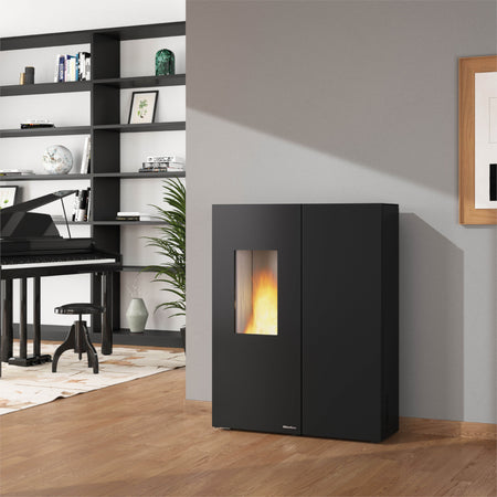 Ambientebild: Extraflame Pelletofen SHARON PLUS STEEL schwarz vor Wand, Flamme sichtbar, Regal, Klavier und Pflanze im Raum | Klimaworld.com