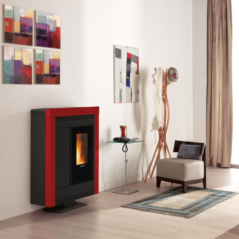 Ambientebild: schmaler Extraflame kanalisierter Pelletofen SOUVENIR PLUS STEEL 5.0 in Bordeaux; im Wohnraum mit Sessel, Teppich und Wandbildern| Klimaworld.com