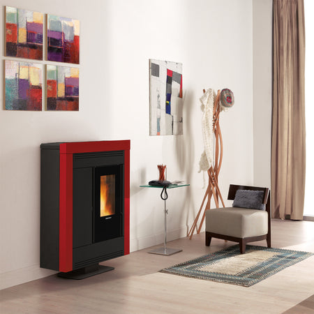 Ambientebild: schmaler Extraflame kanalisierter Pelletofen SOUVENIR PLUS STEEL 5.0 in Bordeaux; im Wohnraum mit Sessel, Teppich und Wandbildern| Klimaworld.com