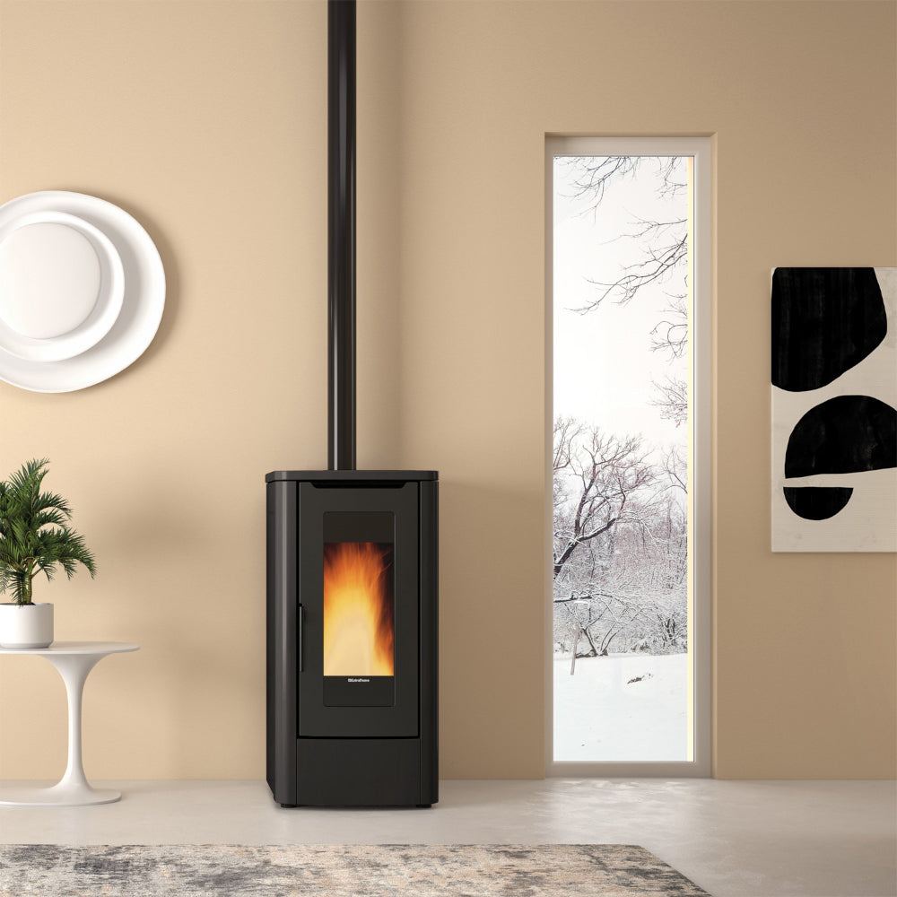Ambientebild: Extraflame beluefteter Pelletofen TEOREMA in Schwarz; in hellem Wohnzimmer neben Fenster mit Blick auf Winterlandschaft | Klimaworld.com