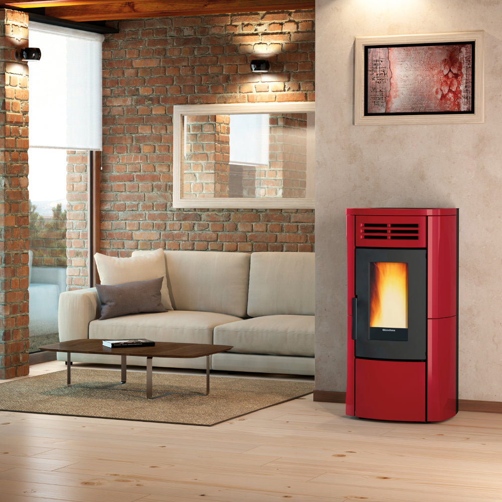 Ambientebild: Extraflame Pelletofen TERRY PLUS in Bordeaux; in modernem Wohnzimmer neben Sofa vor Backsteinwand mit Bild und Fenster | Klimaworld.com