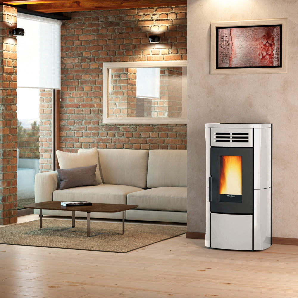 Ambientebild: Extraflame Pelletofen TERRY PLUS in Weiss; in modernem Wohnzimmer neben Sofa vor Backsteinwand mit Bild und Fenster | Klimaworld.com