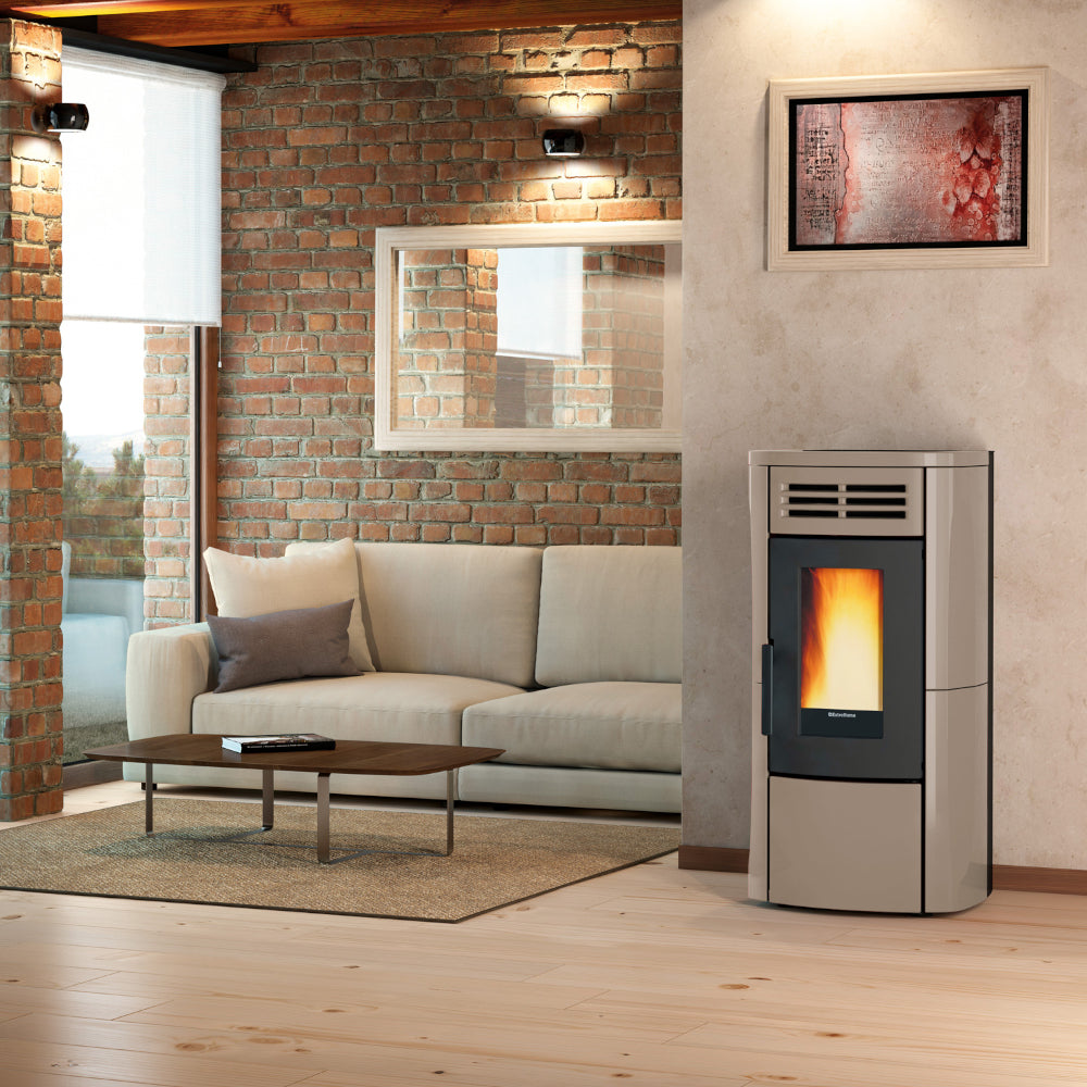 Ambientebild: Extraflame Pelletofen TERRY PLUS in Taupe; in modernem Wohnzimmer neben Sofa vor Backsteinwand mit Bild und Fenster | Klimaworld.com