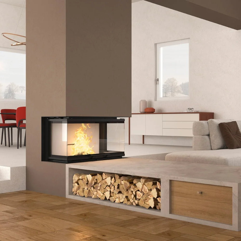 Ambientebild: La Nordica Kamineinsatz MONOBLOCCO 3LC.16 in brauner Wand mit brennendem Feuer, daneben Couch und Holzfach | Klimaworld.com