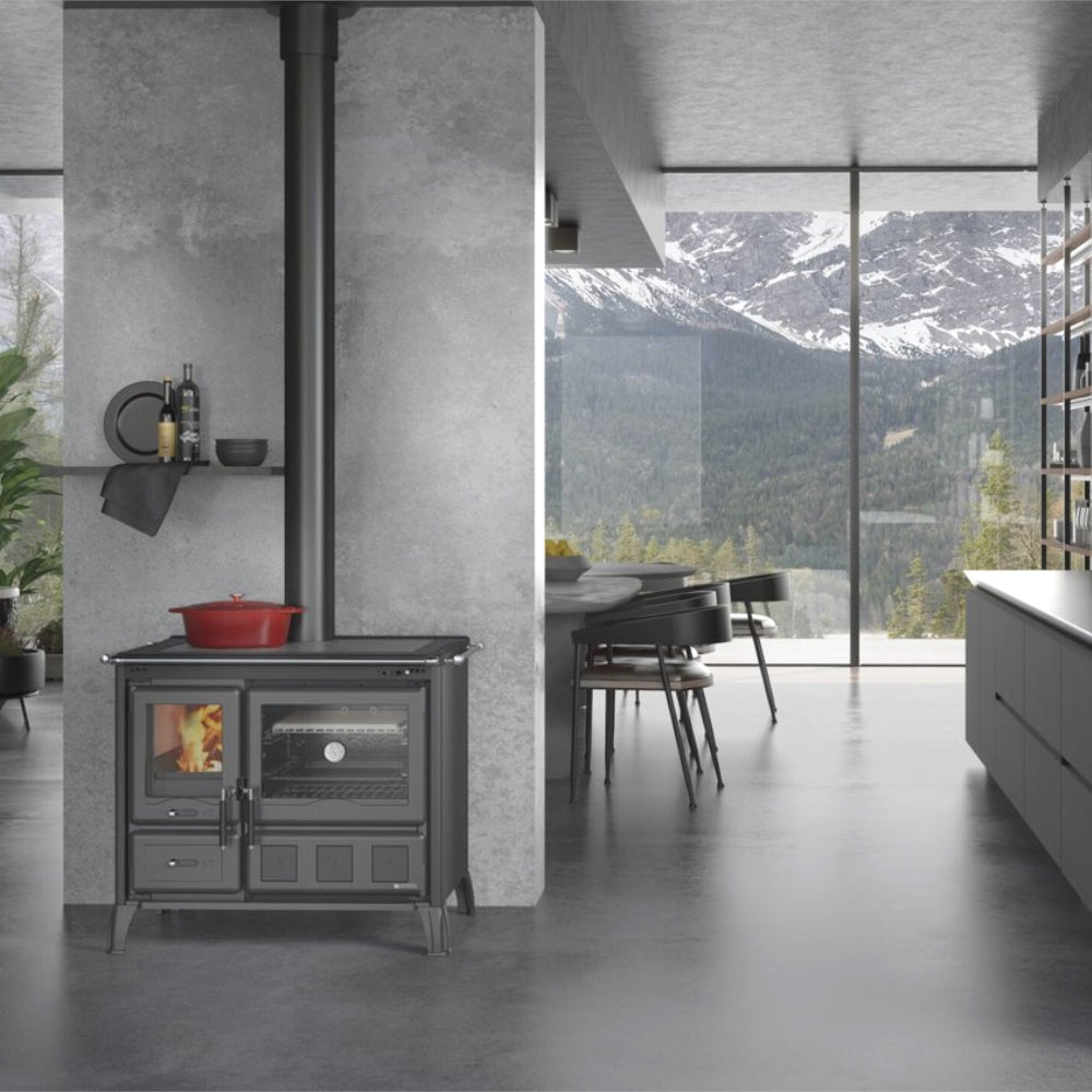 Ambientebild: La Nordica Holzherd GARDENIA XXL STEEL in Anthrazit mit Ofenfenster, Kochplatte und rotem Topf, Bergblick | Klimaworld.com