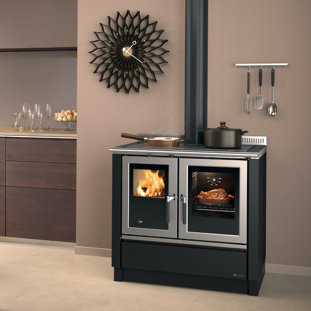 Ambientebild: La Nordica Kuechenofen Venezia in Anthrazit mit sichtbarer Flamme links und beleuchtetem Braten im Backofen rechts | Klimaworld.com