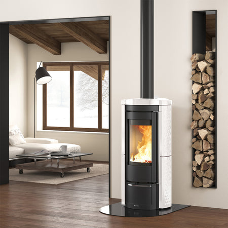 Ambientebild: La Nordica Holzofen LIU' freistehend im Wohnraum, schwarzer Ofen mit weissen Seiten, sichtbares Feuer, Holzregal an Wand | Klimaworld.com