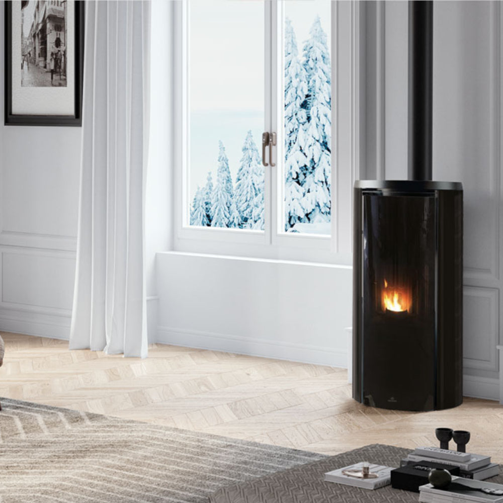Edilkamin Pelletofen CELIA ATC mit schwarzer Seitenverkleidung und durch Magic Glas sichtbaren Feurraum im winterlichem Ambiente | klimaworld.com