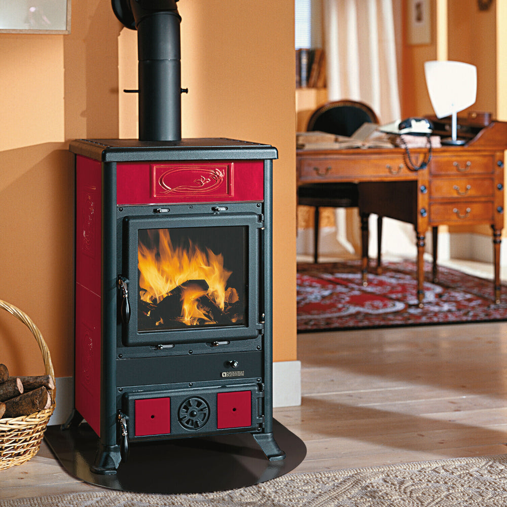Ambientebild: La Nordica Holzofen ROSSELLA R1.16 CERAMICA, Korpus schwarz, verzierte bordeaux Keramikseiten, Glasfenster vorn mit Feuer vor beiger Wand | Klimaworld.com