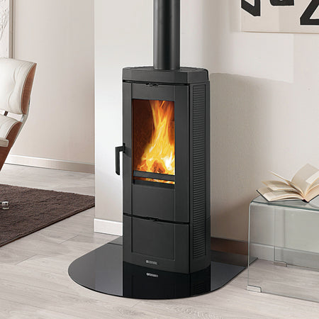 Ambientebild: La Nordica Holzofen CANDY LEAN in Schwarz mit hoher Glasscheibe, sichtbare Flamme, auf runder Bodenplatte im hellen Wohnraum | Klimaworld.com