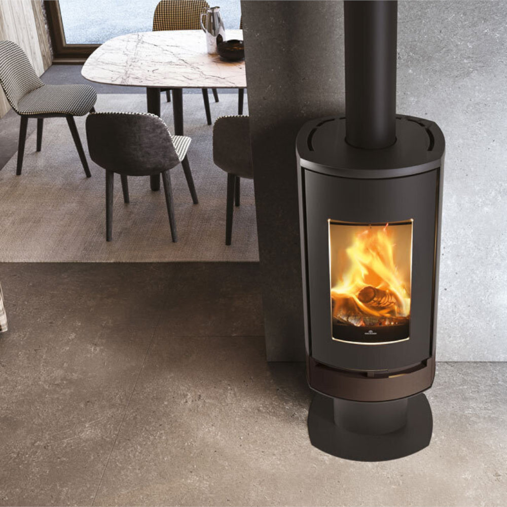 Edilkamin schwarzer Kaminofen CODE J INT mit Flammenbild, untere Verkleidung in Stahl Bronze, stehend auf Sockel in betoniertem Esszimmer | klimaworld.com